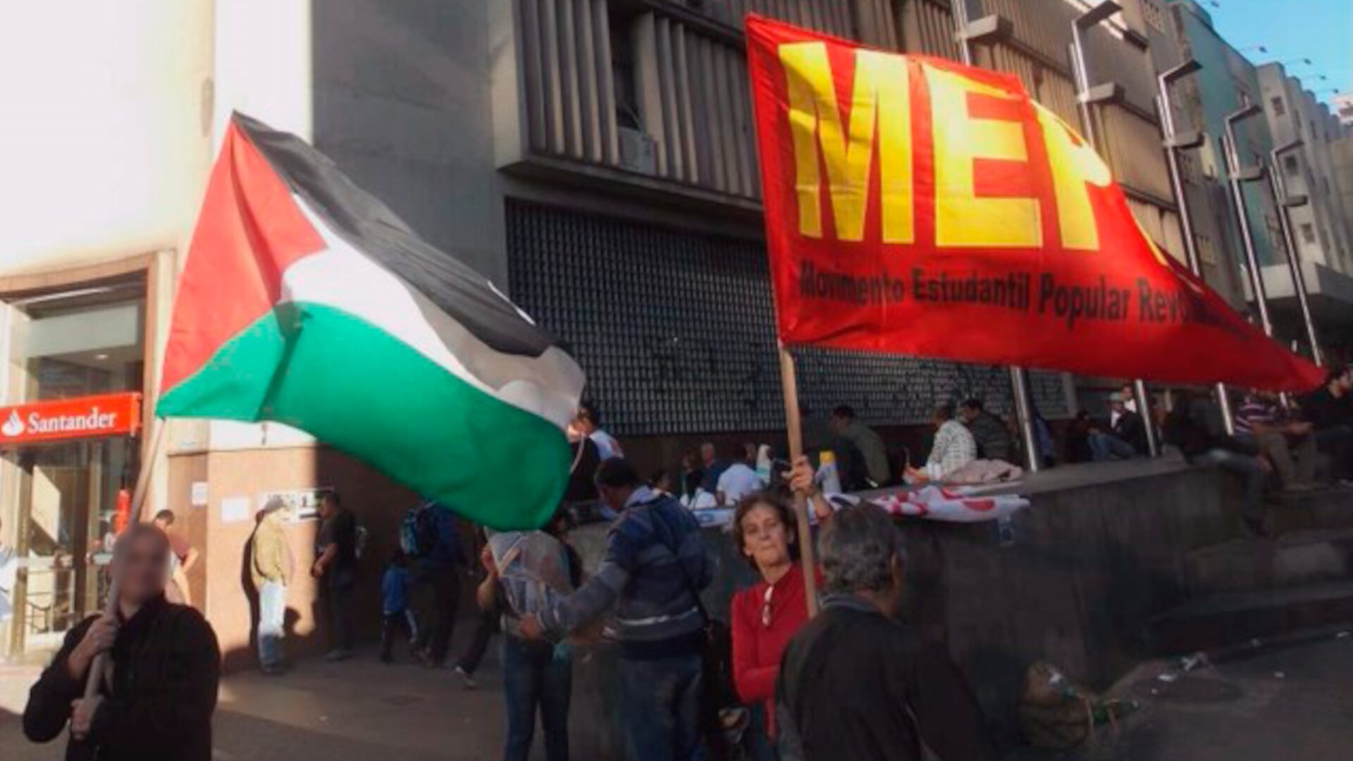 Companheira Sandra Lima, grande revolucionária e heroína do povo, agitando a bandeira do Movimento Estudantil Popular Revolucionário (MEPR) enquanto outra ativista empunha a bandeira da Palestina.